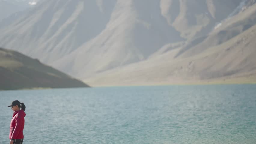 Indian woman traveler in red jacket enjoying serene view of Chandratal Lake, minimal composition and natural mountain light.