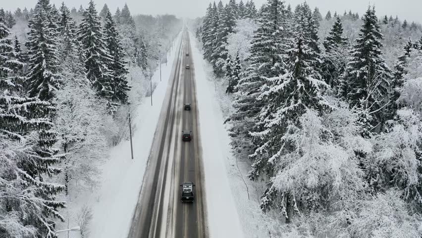 Aerial drone view of a cars driving on slippery and snowy road in winter snow covered forest. Winter landscape, 4k video from above