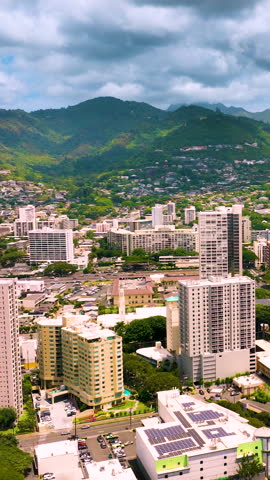 Elevated view of Honolulu, Oahu showing high-rise buildings, solar panels, and dense greenery. The valley setting emphasizes the integration of urban life with nature. Vertical video.