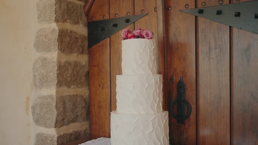 Three tier white wedding cake topped with roses in rustic interior setting