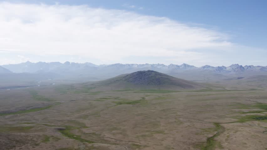 Drone shot of Deosai National Park featuring vast plains, a central hill, and distant mountains. Deosai