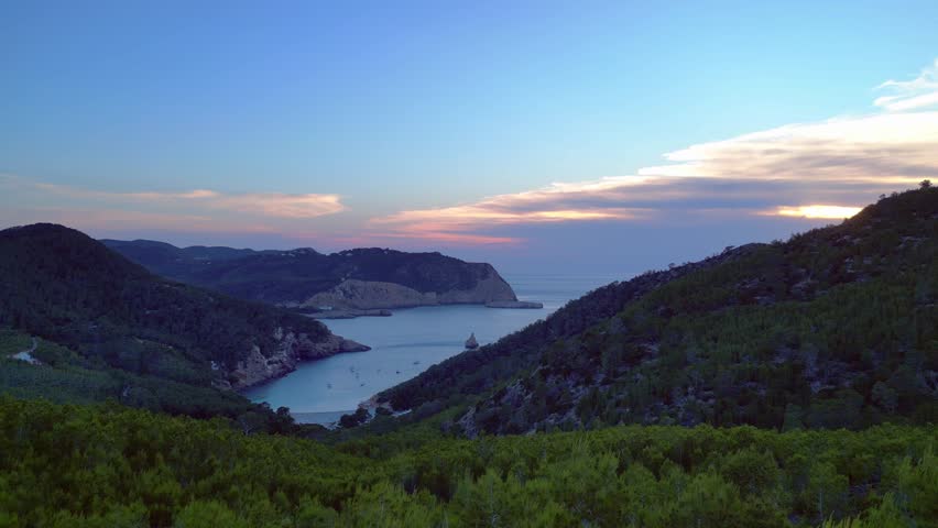 panoramic view of Cala Benirras bay and wooded hills at dusk in Ibiza. Great aerial view flight fly push forward drone