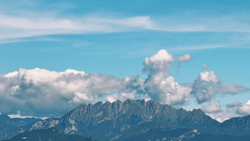 Jagged mountain peaks and clouds formations in a mostly clear cerulean sky