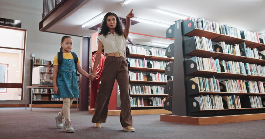 Walking, child and holding hands with woman, library and happy for knowledge development and growth. Pointing, tutor and searching for books with girl, education and smile for scholarship opportunity