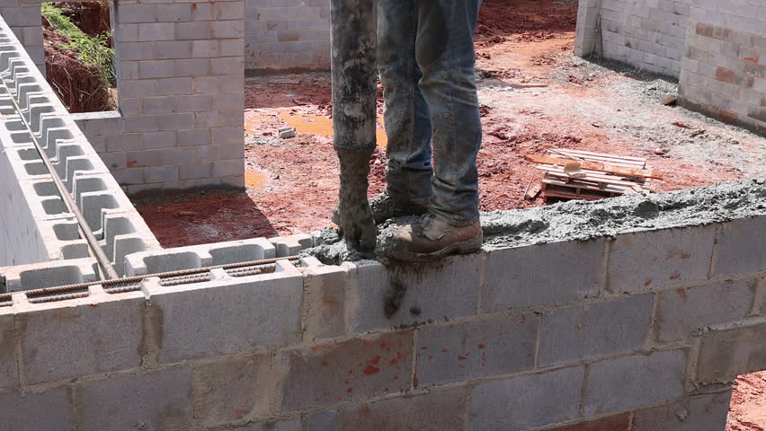 Construction worker fills cinder block wall with concrete using cement pipe pump while working on new building