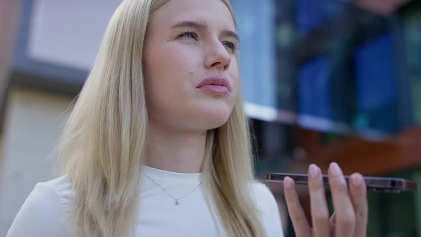 Close-up of young woman holding smartphone in front of her mouth, speaking clearly to record a voice message or use speech to text.