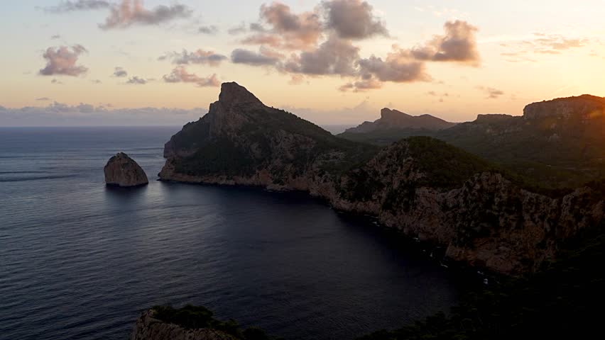 
Peaceful sunrise over Cap de Formentor cliffs in Mallorca, Spain. Soft morning light illuminates rocky coast and calm Mediterranean Sea.