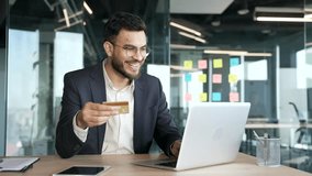 Smiling businessman in a formal suit enters a credit card data on a laptop sitting at a workplace in a business office. Handsome man shopping online, happy about a successful transaction, e-commerce - Powered by Shutterstock - Get 15% off with code: PIKWIZARD15