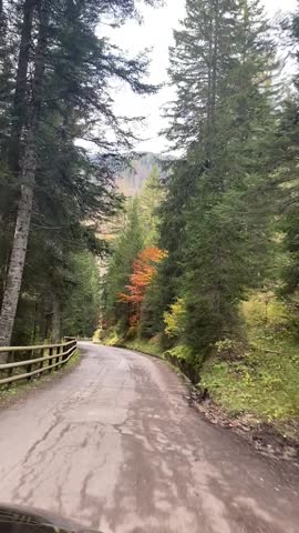 Driving on autumn rural road in Dolomites Italy under cloudy sky