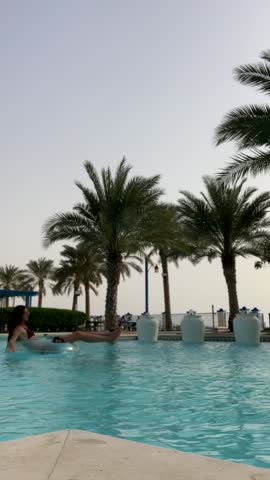 A girl floats on an inflatable ring in a pool. Relaxing in the pool against a backdrop of palm trees. A beautiful European girl in the pool.