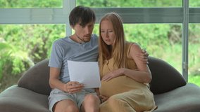 Pregnant woman and her husband sitting on a couch looking worried while reading a scary document in a paper held by the man. Slowmotion video. - Powered by Shutterstock - Get 15% off with code: PIKWIZARD15