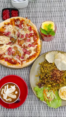 A flat lay view of lunch set that consists of pizza, fried rice, non-alcoholic mojito, and hot cappuccino on the table.