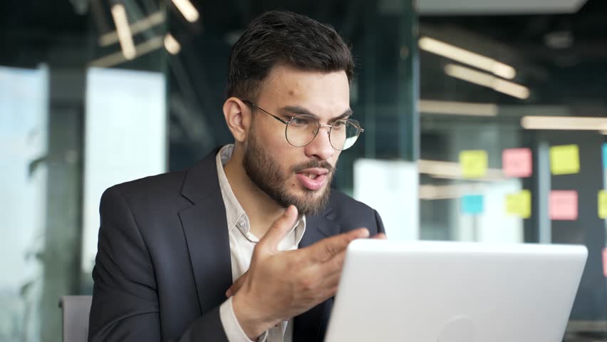 Confident businessman in a formal suit talking on a video call using a laptop at workplace in office. Entrepreneur has a business meeting. Manager speaks remotely at an online conference. Close up