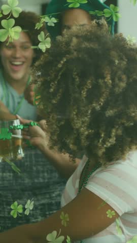 Animation of clovers over happy diverse friends wearing clover shape items and drinking beer. social media and st patrick