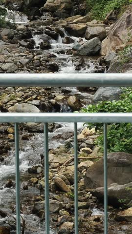 Wild mountain river. view from the top, through the metal fence of the bridge. fast small mountain river with crystal clear water. Rapid water flow running through stone rapids and over the stones in 