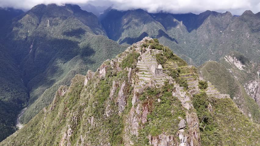 A dynamic shot circles the steep peak of Huayna Picchu at Machu Picchu, revealing the ancient stone stairs leading to the summit and the intricate structures and terraces built into its cliffsides