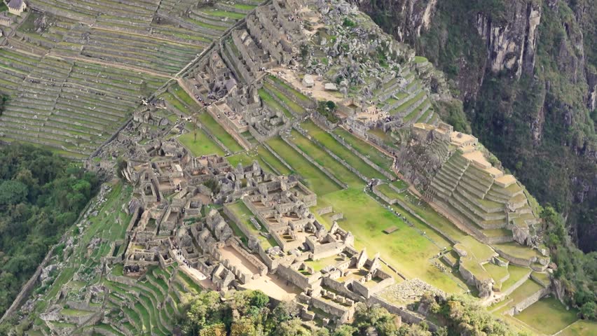 A close-up, downward-facing shot begins in the industrial zone of Machu Picchu, then flies smoothly over the site to reveal the intricate patterns of the ancient cultivation and agricultural terraces