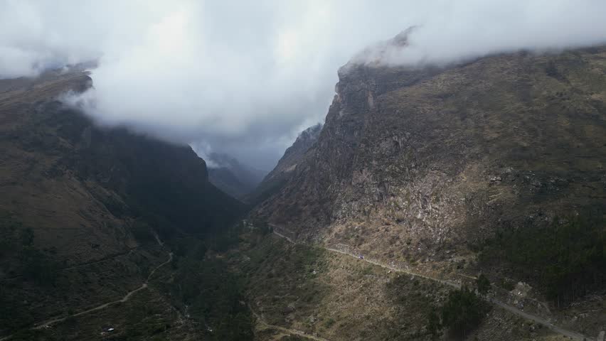Huaraz, Peru: Orbit drone footage of car on the valley road to Punta Olimpica in Huascaran National Park in the Cordillera blanca mountains under dramatic cloudy sky