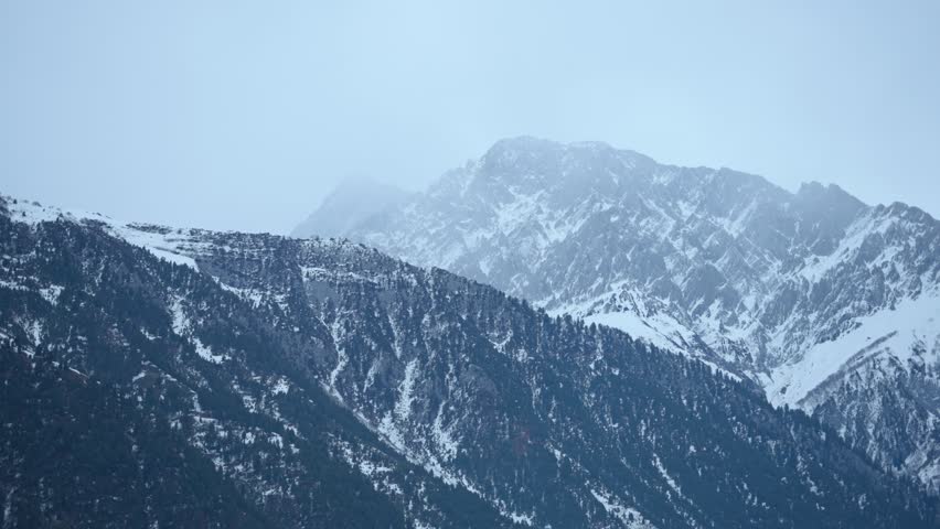 4K Landscape shot of snowy Himalayan mountain peaks during a winter storm as seen from Sonmarg in Jammu and Kashmir, India. Scenic view of snow clad mountain peaks with pine trees on top of them. 