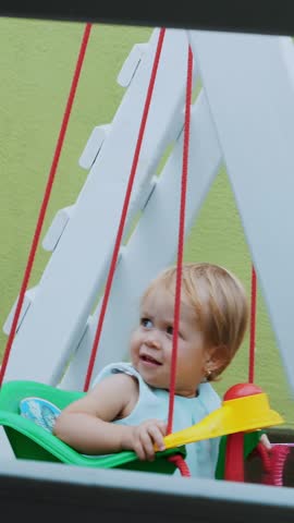 Nice little one year-old girl swinging on a swing in the playground.