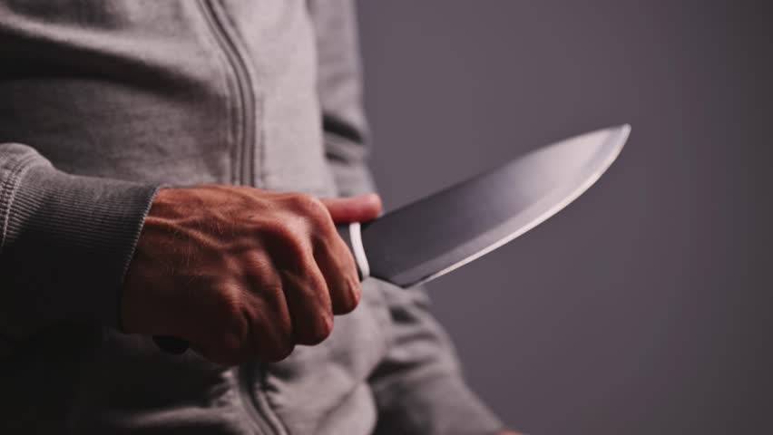 Man wearing gray hoodie holding large kitchen knife in hand, low key lighting, danger and crime concept. 4K with selective focus.
