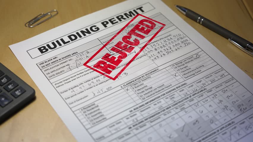 Close-up of a rejected building permit stamped in red ink on a desk with pen and paper clips, symbolizing construction denial or zoning issue. Fictional data. 14916  	