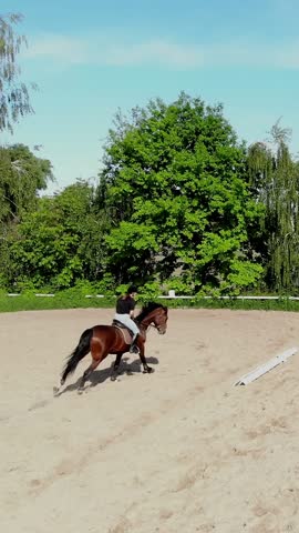 Riders, jockeys ride horses, perform various exercises with horses, next to barriers. summer, outdoors, view from above, aerial video shooting, training sand field, playground