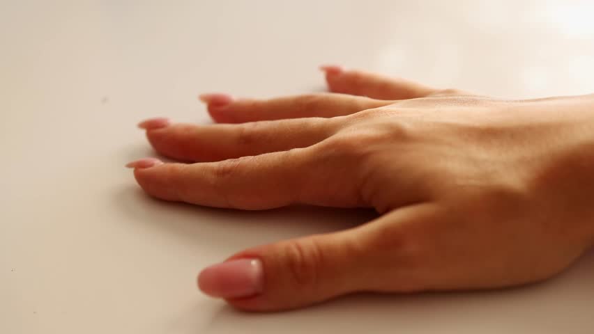 Female hand with manicure tapping rhythmically on white surface.