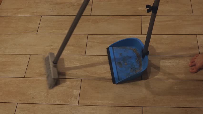 Close-up of cleaning with a plastic dustpan and broom.