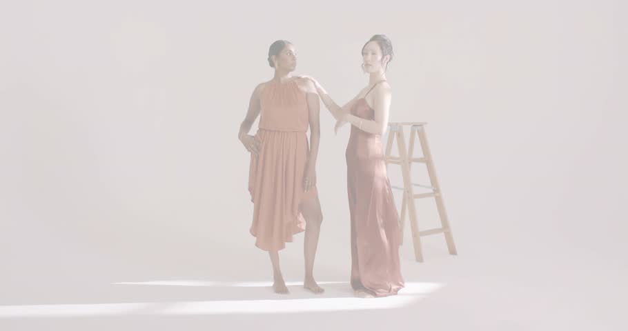 Teal glow emerging behind models by ladder forming swirling halo with models shifting fashion poses. Fashion, elegance, runway, glamour, monochrome, contemporary, artistic