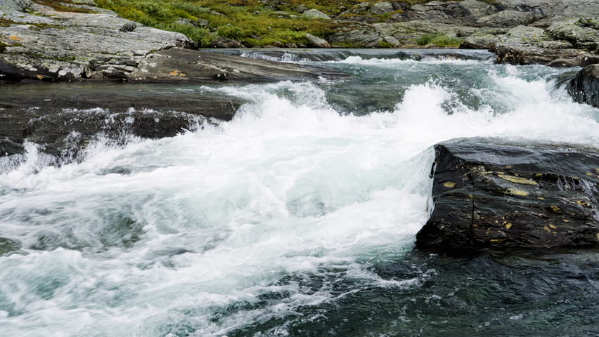 Turbulent stream of a wild mountain river cascading over dark, mossy rocks in the scenic landscape of Stekenjokk, Sweden, creating powerful white water rapids and beautiful cascades