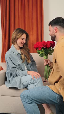 A delighted woman smiles as she receives a stunning bouquet of red roses from her partner, showcasing a moment filled with love and affection in a cozy indoor space, perfect for romantic occasions.