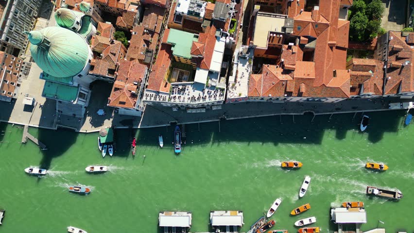 Static aerial drone shot hovering high above the Grand Canal in Venice, Italy. View captures boat traffic, Vaporetti, and historic buildings along the busy waterway on a sunny summer day.