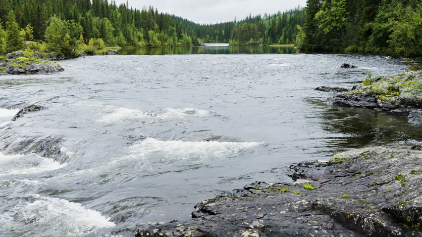 Beautiful scenic view of the waterfall, where the Kultsjoan river flows over wide, stair like rock formations surrounded by the lush green forests of northern Sweden
