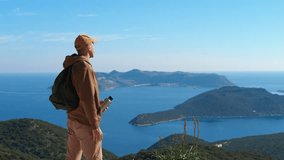 Hiker drinking water looking at ocean view from mountain top. Young male hiker drinking fresh water, pausing during mountain trek, enjoying panoramic ocean view with blue sky and distant islands - Powered by Shutterstock - Get 15% off with code: PIKWIZARD15
