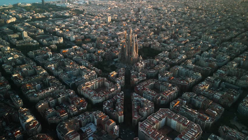 4K drone aerial view of Sagrada Familia in Barcelona at sunset, showing golden light over Eixample district and iconic grid city pattern, Catalonia, Spain