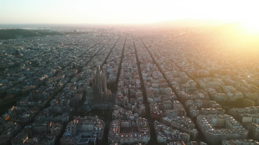4K drone aerial view of Sagrada Familia in Barcelona at sunset, showing golden light over Eixample district and iconic grid city pattern, Catalonia, Spain
