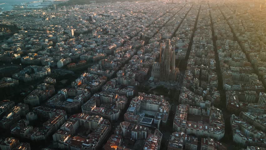 4K drone aerial view of Sagrada Familia in Barcelona at sunset, showing golden light over Eixample district and iconic grid city pattern, Catalonia, Spain
