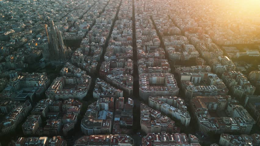 4K drone aerial view of Sagrada Familia in Barcelona at sunset, showing golden light over Eixample district and iconic grid city pattern, Catalonia, Spain