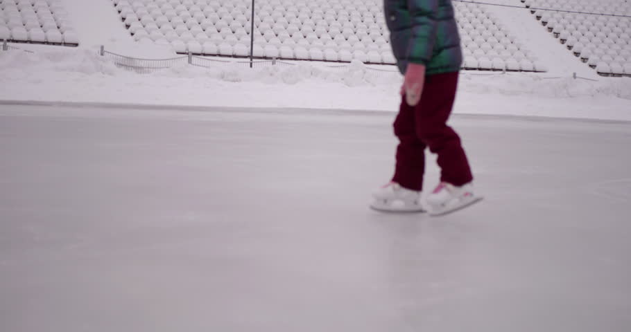 Young girl in warm winter clothes takes first steps on ice rink learning to skate showing joyful winter outdoor activity healthy motion and playful experience on frozen surface in cold season