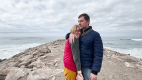 Happy middle-aged couple stands on a rocky breakwater by the Atlantic Ocean. They talk, kiss, and embrace lovingly, enjoying a romantic moment together under a cloudy sky near the sea - Powered by Shutterstock - Get 15% off with code: PIKWIZARD15