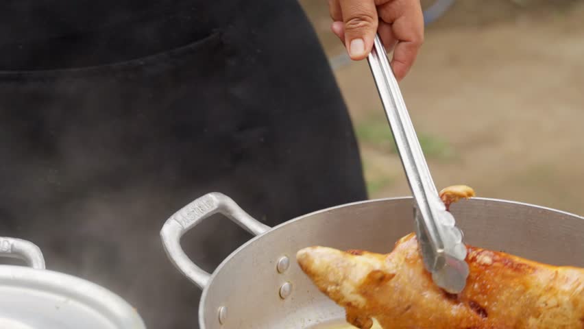 Close up of a chef using tongs to deep fry a whole guinea pig in a pot of hot oil. Traditional peruvian cuisine being prepared outdoors