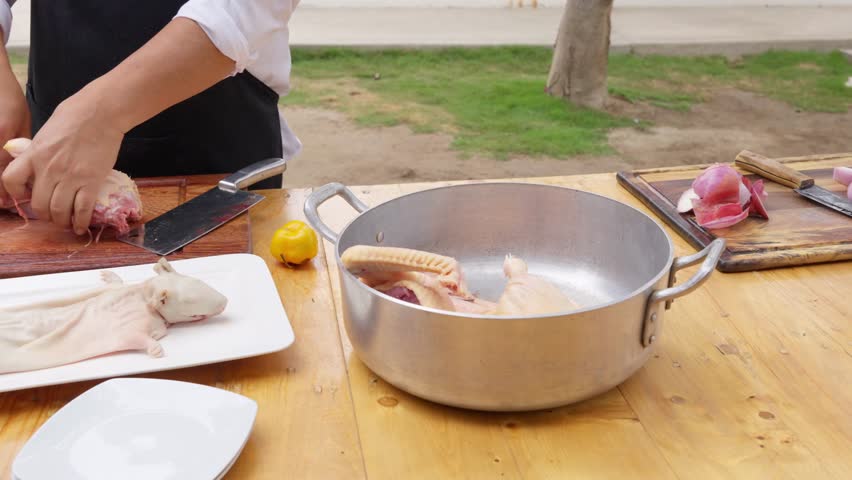 Professional chef cutting raw duck meat with a cleaver for a traditional peruvian recipe. A whole guinea pig rests on a plate nearby