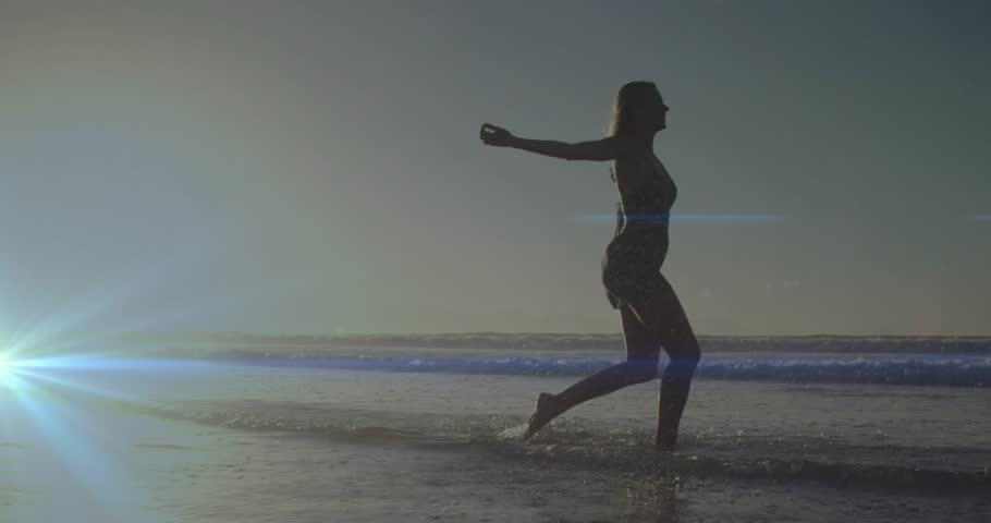 Stepping into shallow ocean water woman performing rhythmic leg lifts and kicking water for travel. Ocean, coastal, serenity, movement, sunset, leisure, harmony