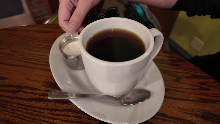 Pouring creamer into a cup of coffee