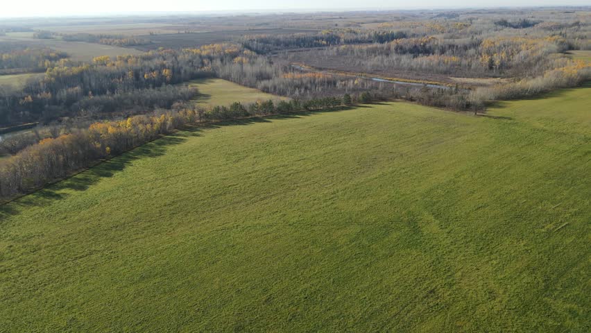 Drone airborne view looking down at farmland and a winding river surrounded by autumn trees with a mix of colors and leafless