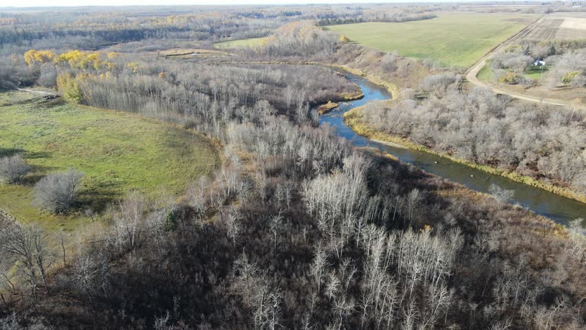 Drone airborne view looking down on a winding river surrounded by leafless trees and fall colors