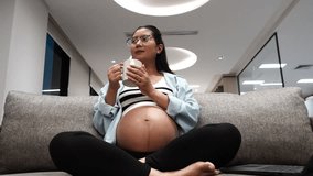 Eight months pregnant Asian woman sits on a sofa drinking calcium-fortified milk in a condominium. - Powered by Shutterstock - Get 15% off with code: PIKWIZARD15