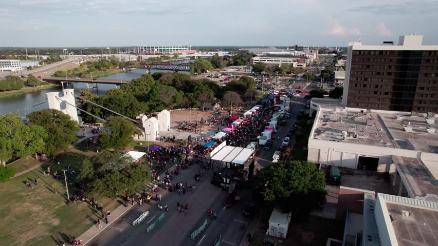 4K parallax drone footage of the Waco Suspension Bridge during the Día de los Muertos festival, capturing colorful decorations, vibrant crowds, and city scenery.