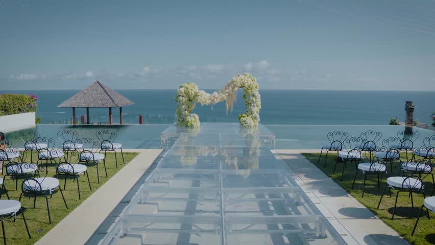 A seaside wedding setup with a floral arch by the pool facing the blue ocean view.